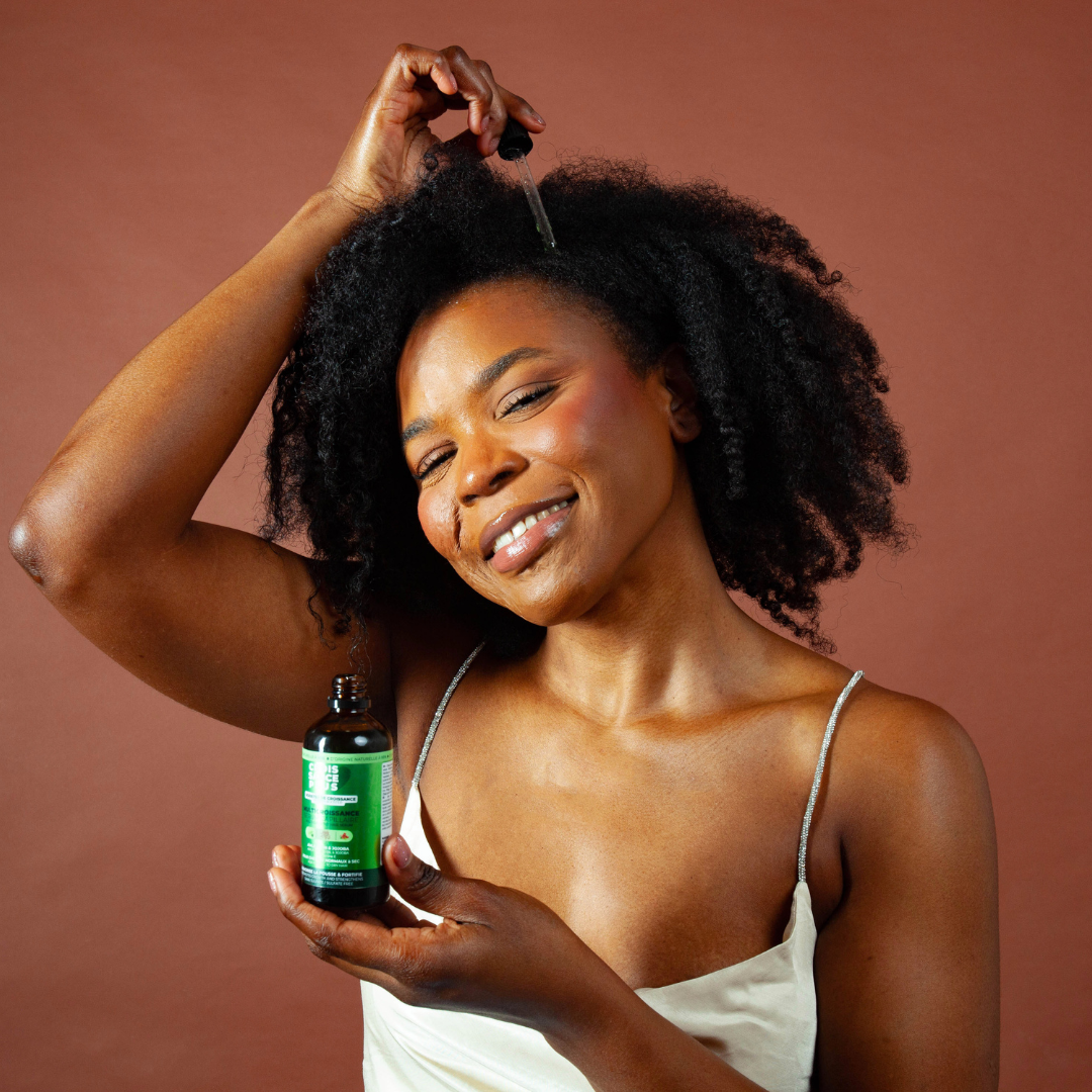 Smiling Black woman applying organic hair growth serum "Croissance Plus - Multricroissance Serum Capillaire" to her natural curly hair by JS Organics.